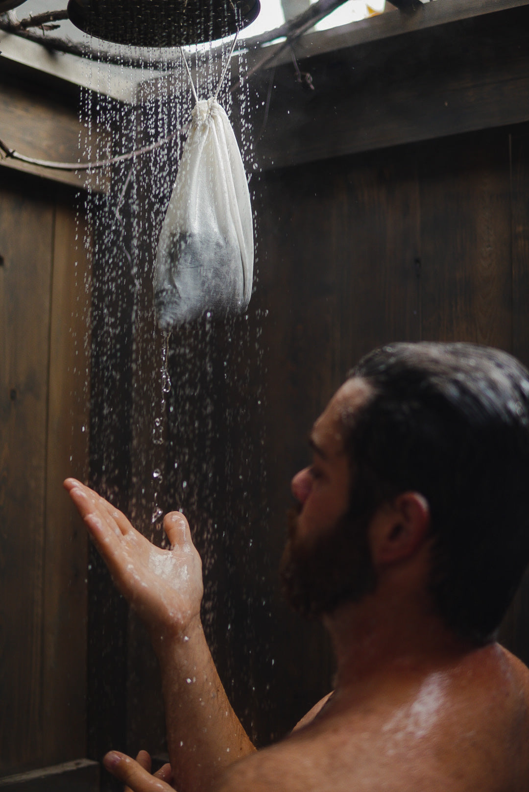 Man standing in an outdoor shower with a Nautical Farms Rose and Kelp Bath Soak hanging from the shower head. Sustainable Maine Seaweed Company.