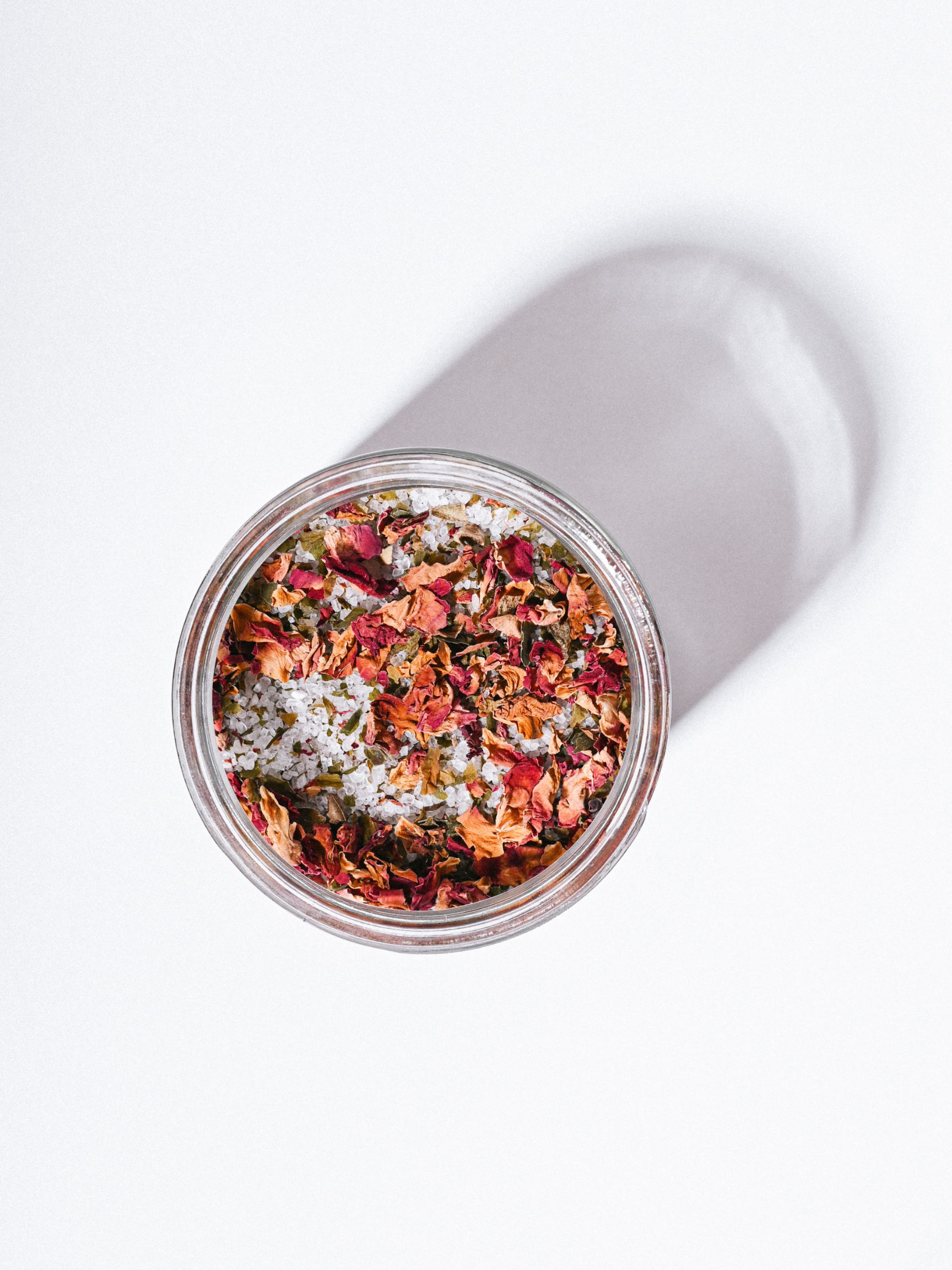 Jar of red dried roses, organic kelp, and sea salt on a white background